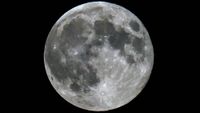 A photo of a full moon shining in a black sky, with dark lunar seas and bright craters visible on its surface.