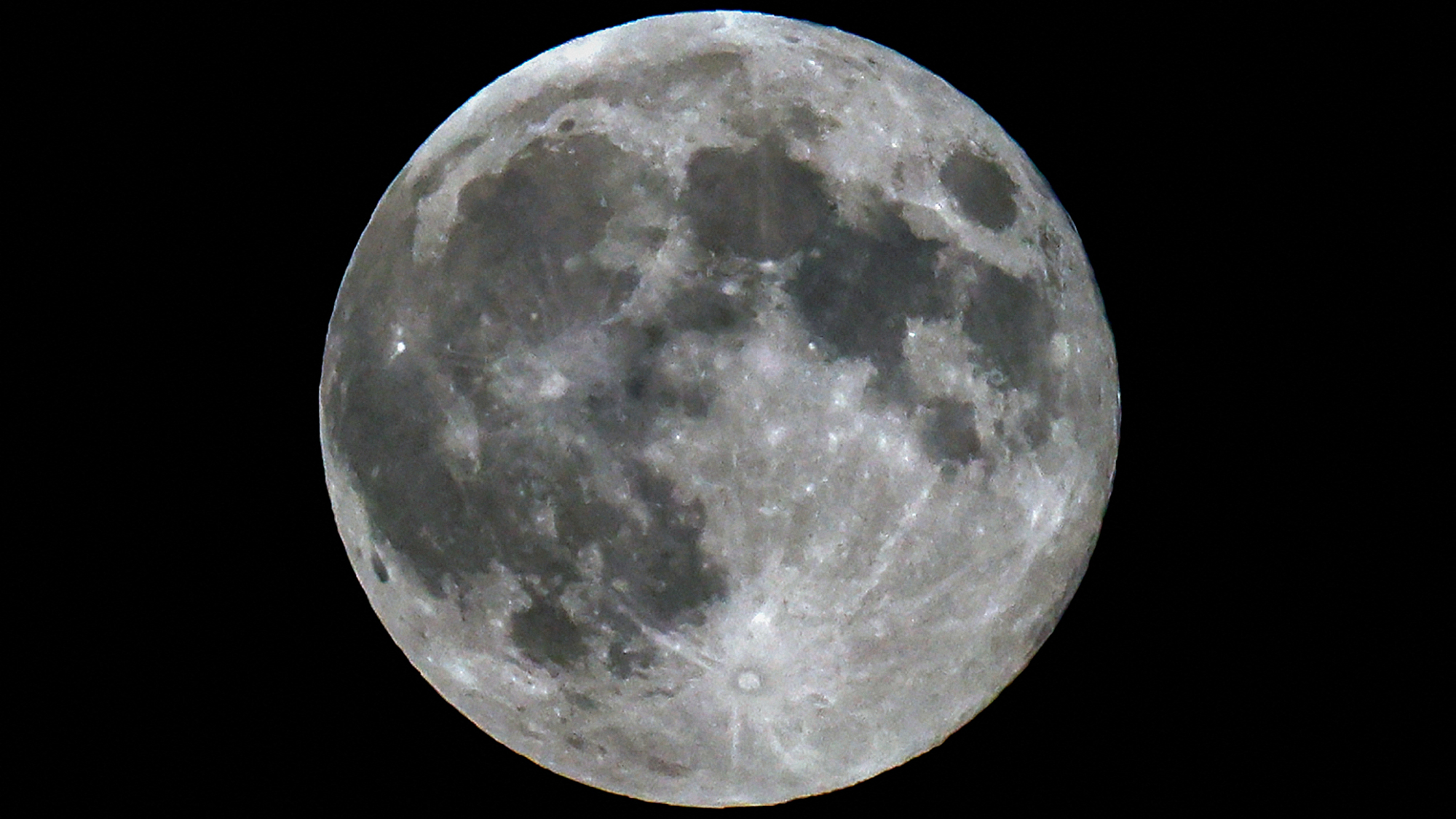 A photo of a full moon shining in a black sky, with dark lunar seas and bright craters visible on its surface.