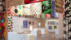 A large showroom with brightly patterned IKEA textiles hung from the ceiling and white display stands with glass cloches holding textiles and art