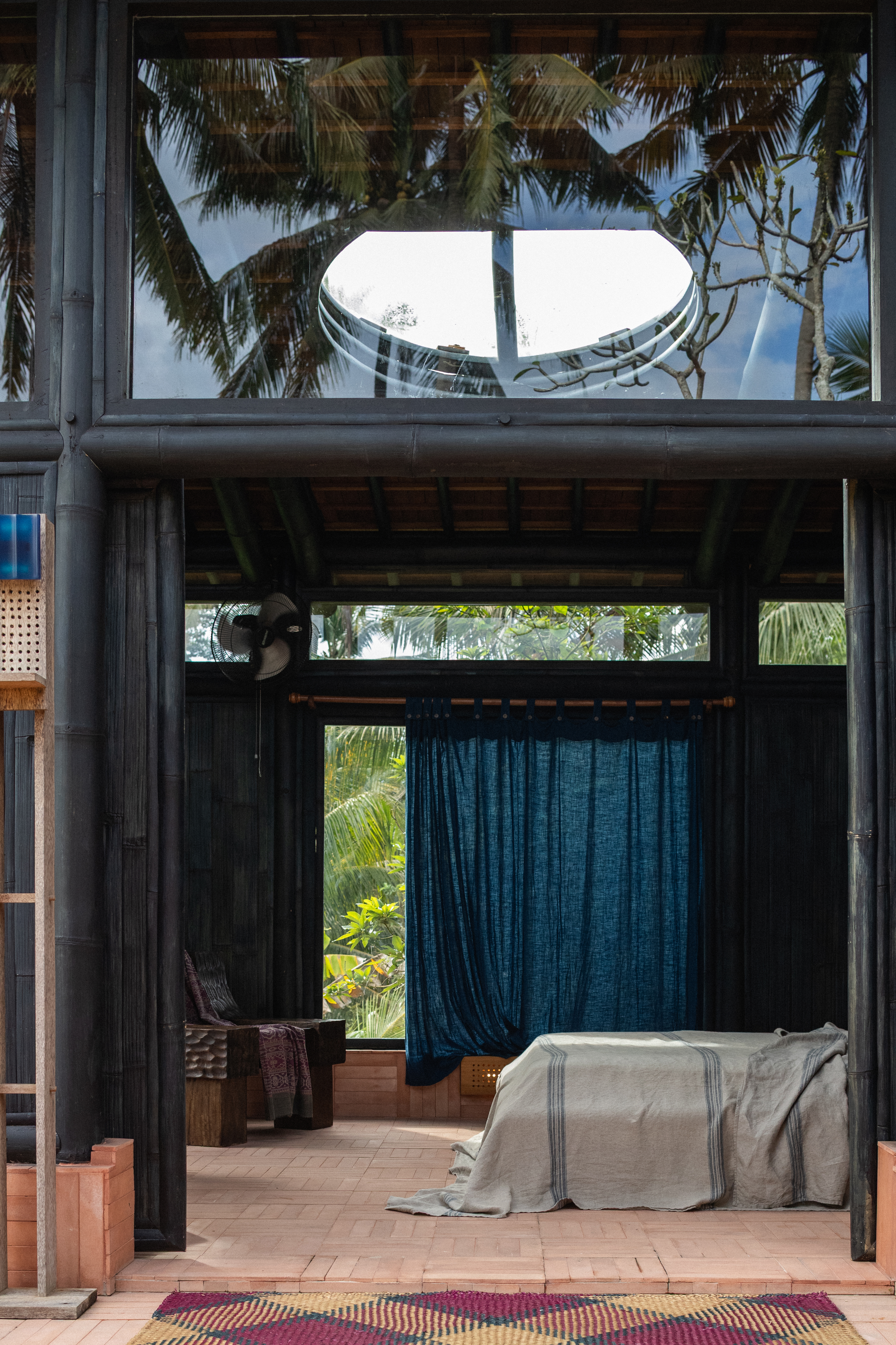 Interiors of a tropical hotel with curved passageways, terracotta walls, colorful curtains, woody furniture, color pops, and nature all around.