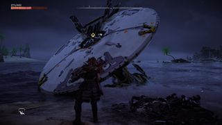 Aloy stands in front of a broken down Tallneck that is in the sea.