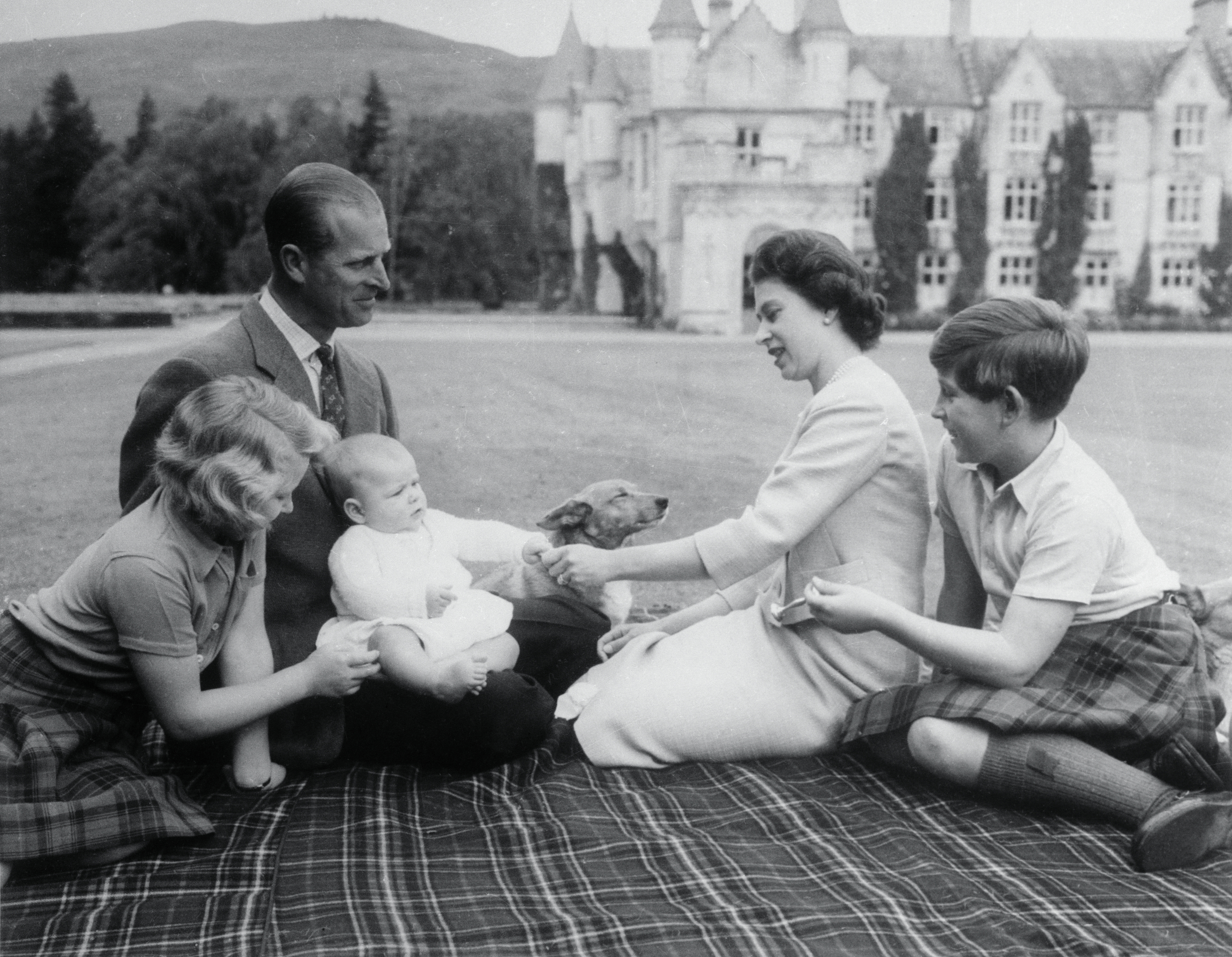 Baby Prince Andrew perches on Prince Philip's lap during a picnic on the grounds of Balmoral Castle. Looking on are Queen Elizabeth, Prince Charles, and Princess Anne.