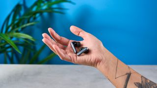 a pair of silver and black shiny earbuds with a black matte charging case are photographed against the Tom's Guide blue background