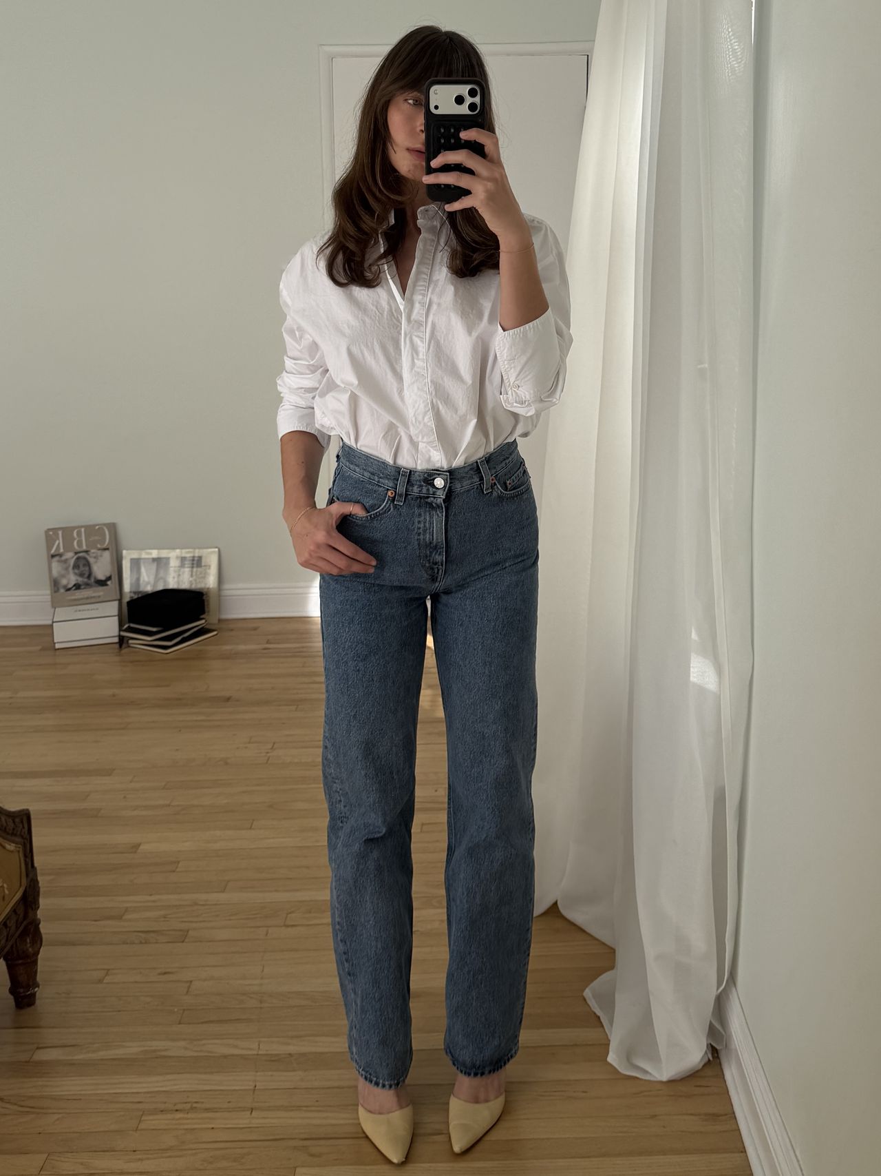 Kathryn Zahorak posing in mirror wearing white button-down shirt, jeans, and heels