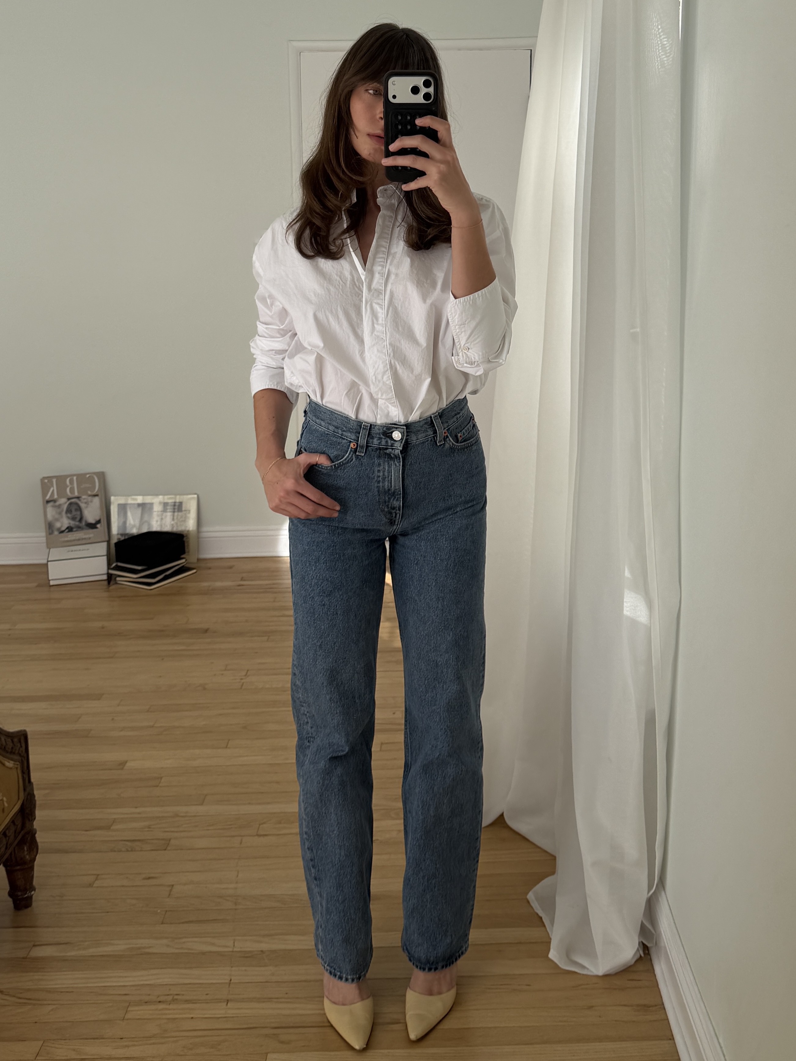 Kathryn Zahorak posing in mirror wearing white button-down shirt, jeans, and heels 