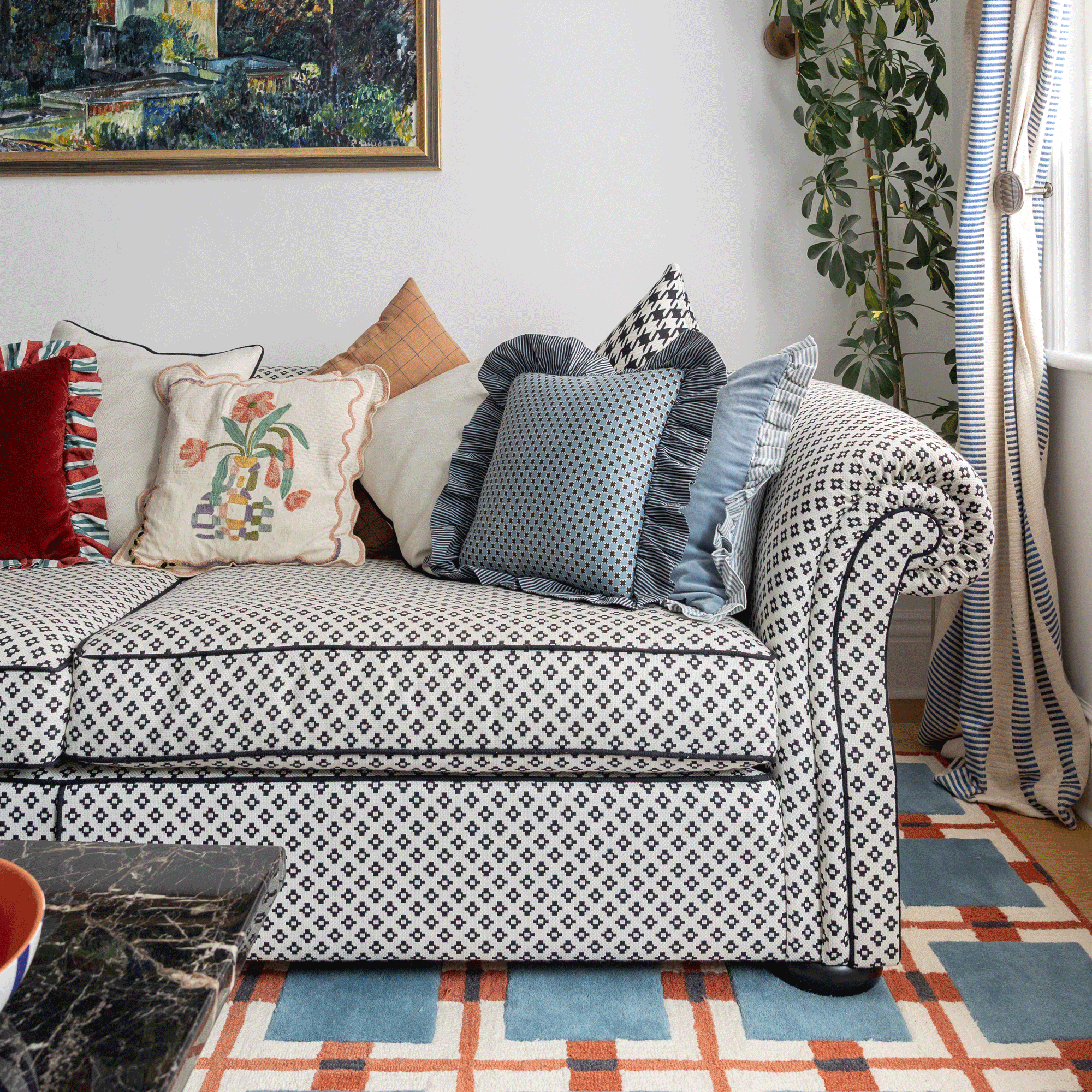 a living room with a black and white patterned sofa a blue red and cream patterned rug and striped curtains