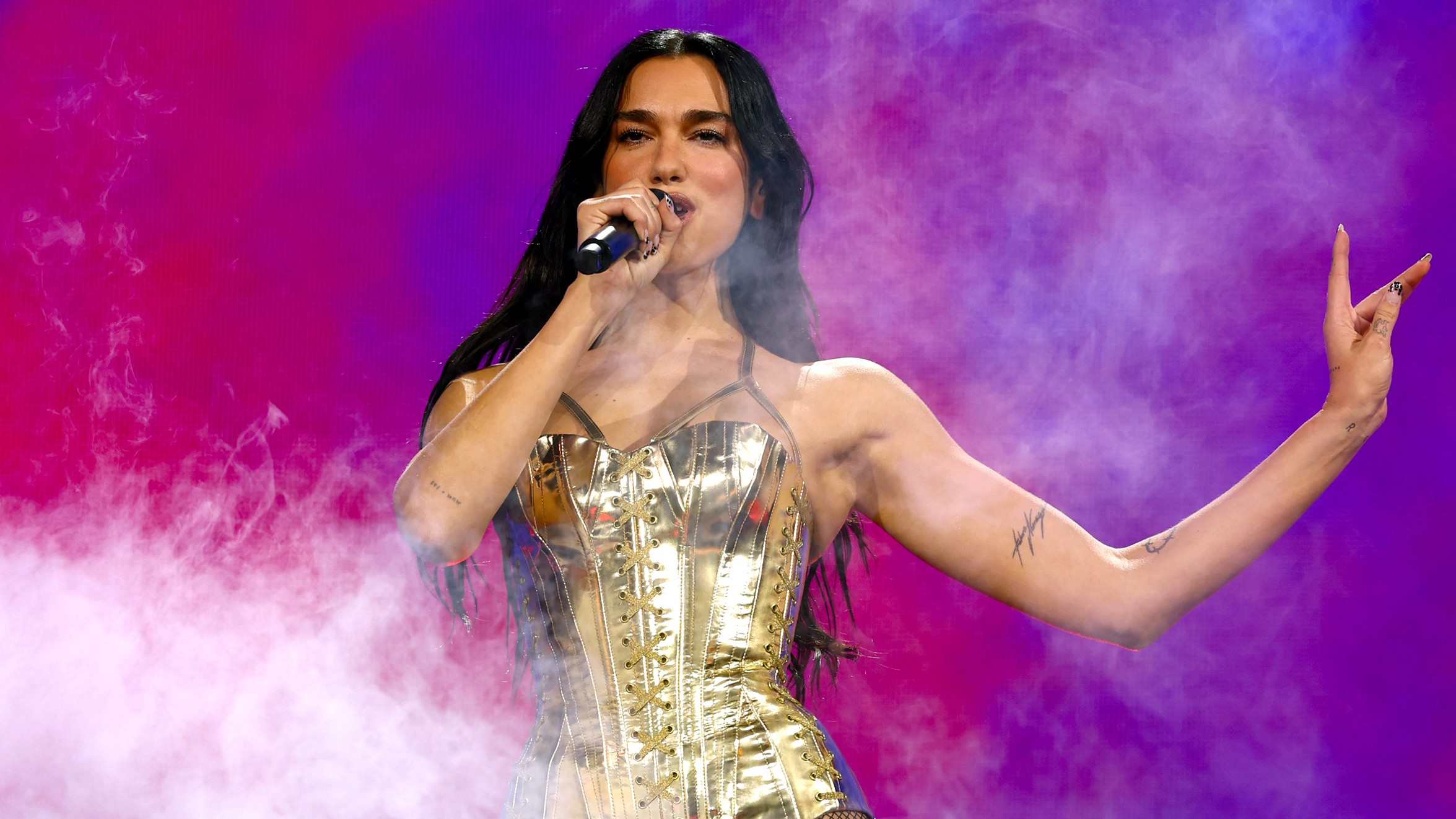 a woman with dark hair performing on stage at a concert in a metallic gold leotard