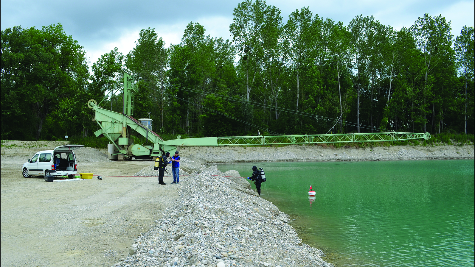 people work at the edge of a river with gravel on the shore