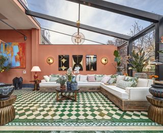 An orangery painted in a soft orange colour with green and white checkerboard tiled flooring and a corner sofa with pattered cushions