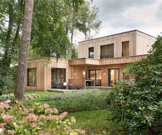 A modern timber-clad self build with multiple flat roofs, set on a woodland plot