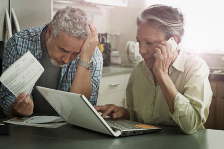 Two people look worried while on a computer and the telephone. 