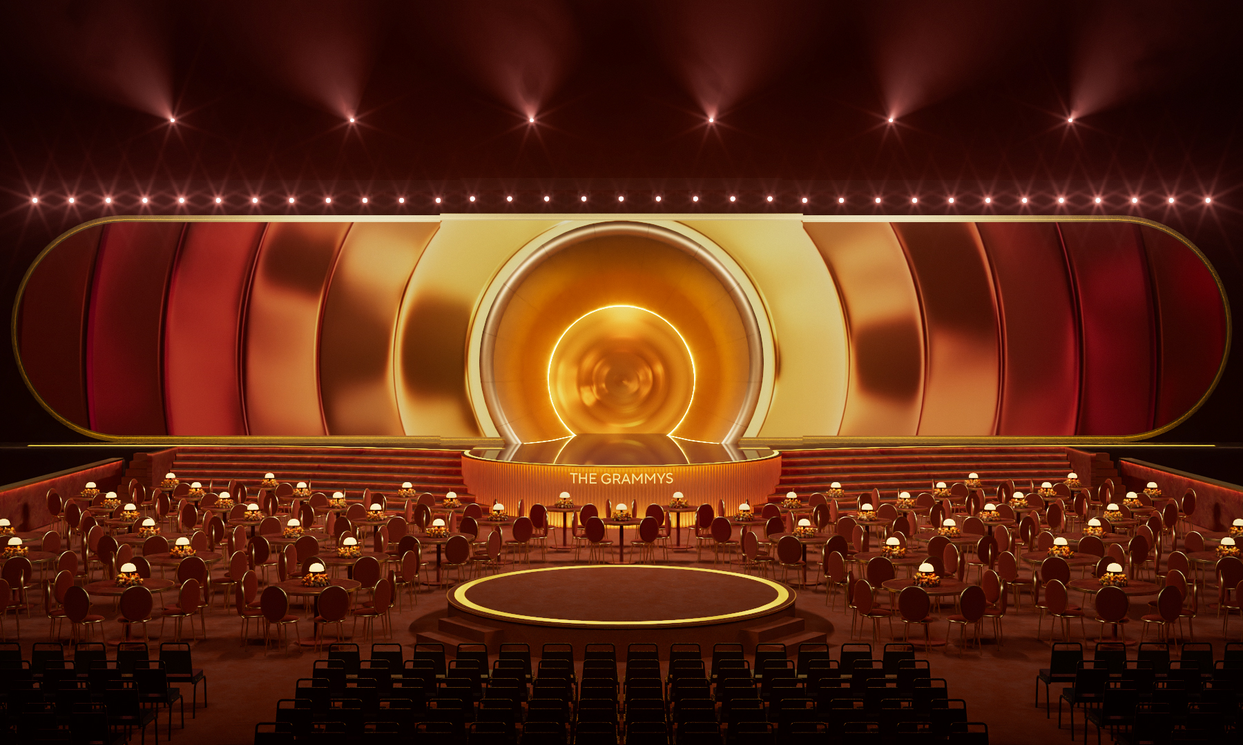 An aerial view of a performance stage with a sculptural, abstract structure of orange, red, and yellow swathes, foregrounded by a series of ceremony round tables with lamps as centerpieces.