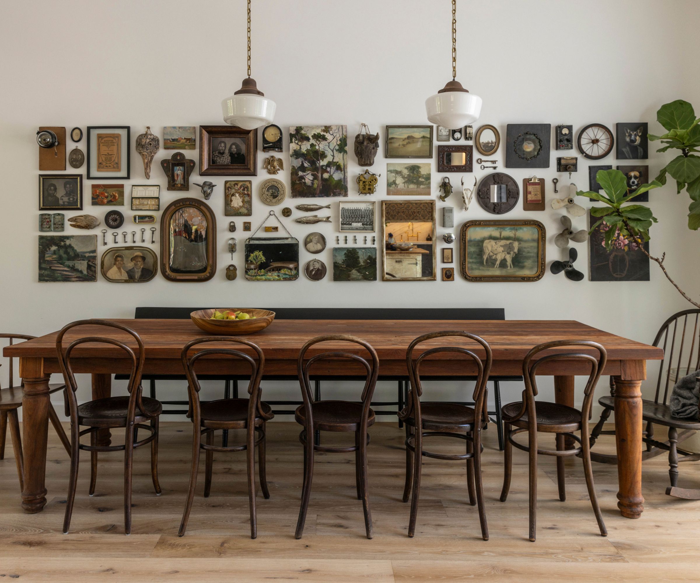 Dining room with long wood table, vintage bistro chairs, pendant lights and gallery wall with vintage frames and paintings