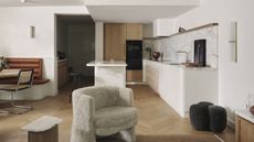 A broken plan kitchen diner with a peninsula island, banquette seating, and an armchair in the foreground