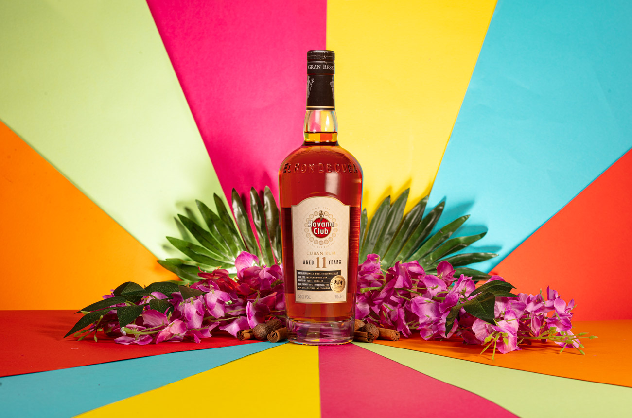 A bottle of rum and some flowers with a rainbow background
