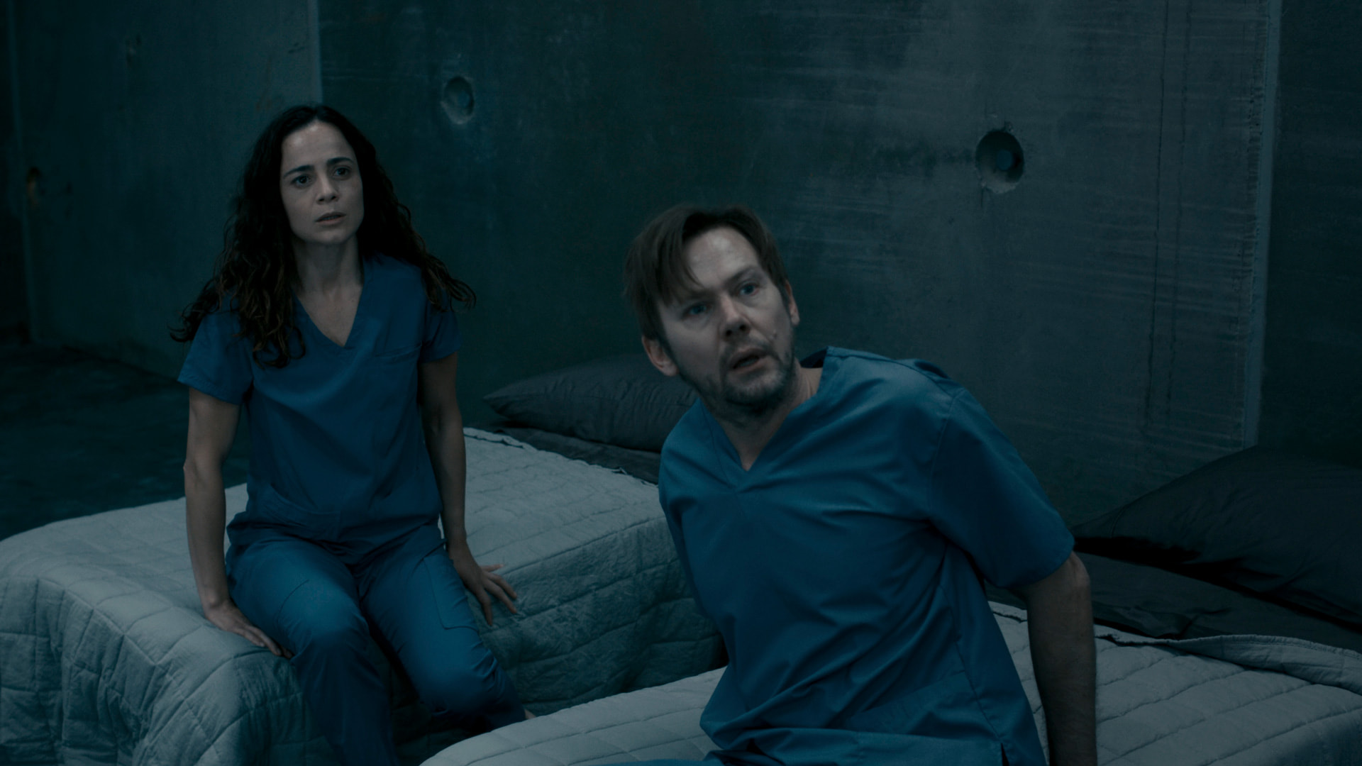 a woman and a man in blue hospital outfits sitting on beds