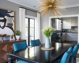 Open-plan kitchen and dining room, gray painted walls, wooden dining table, blue chairs, metallic pendant light
