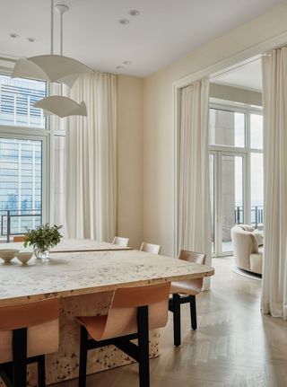 The dining room of a light-filled Manhattan apartment, featuring a natural stone table and wooden dining chairs