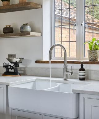 A kitchen with white and grey quartz worktops, stainless steel faucet, and reclaimed wood shelves