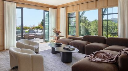 Modern living room with large window, brown couch and cream chairs