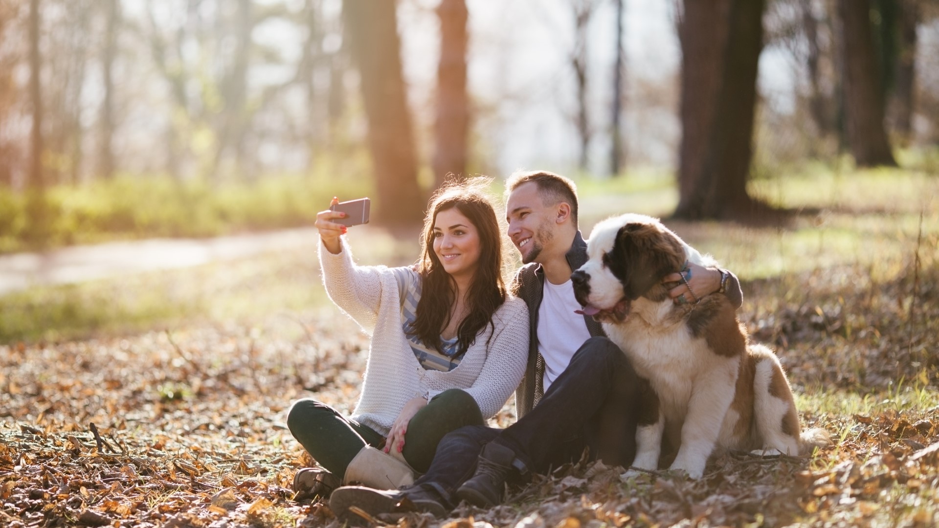 A couple takes a selfie with a Saint Bernard in the park