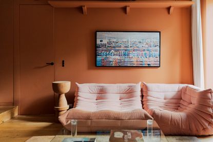 A living room with orange walls and a pink Togo sofa