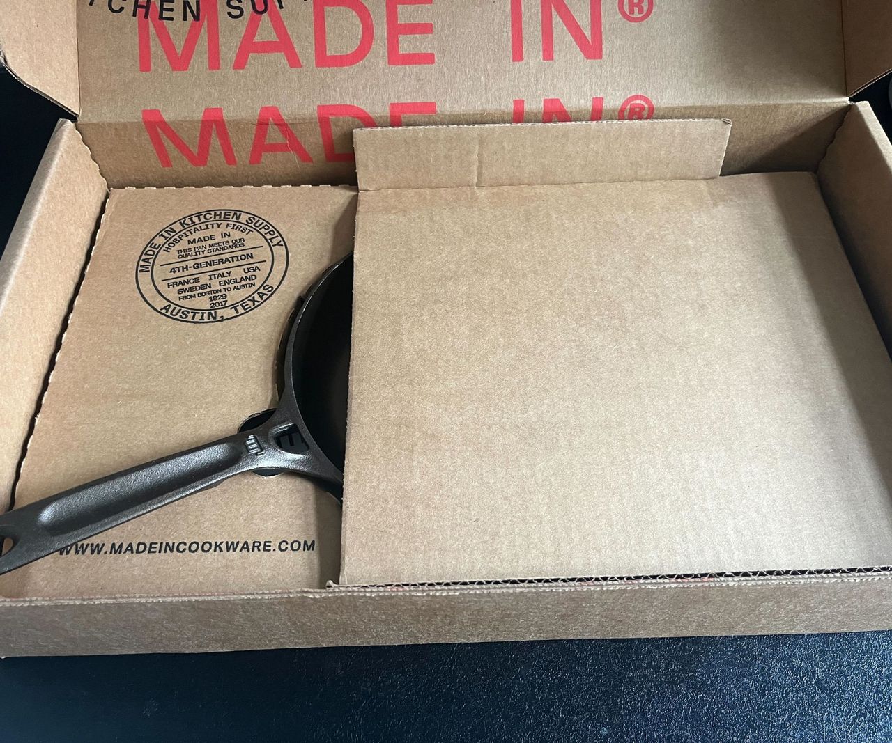 A Made In cookware cardboard box on a black kitchen counter with half a small skillet visible.