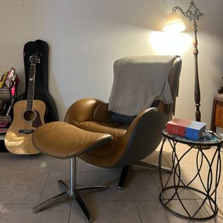 NOUHAUS massage chair with matching ottoman in an apartment beside a guitar, table, and shelf