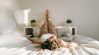 A woman lying on her back on bed with her legs raised against the wall as she naps