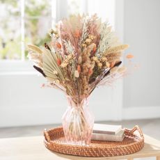 Bunch of dried flowers in glass vase on woven tray