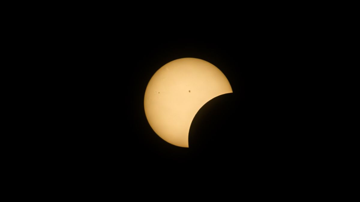 partial solar eclipse shows the moon taking a &quot;bite&quot; out of the sun while some small black sunspots are visible on the sun&#039;s surface.