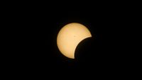 partial solar eclipse shows the moon taking a "bite" out of the sun while some small black sunspots are visible on the sun's surface.