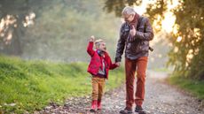 A grandfather holds his grandson's hand as they walk down a country path. They are looking at each other and smiling.