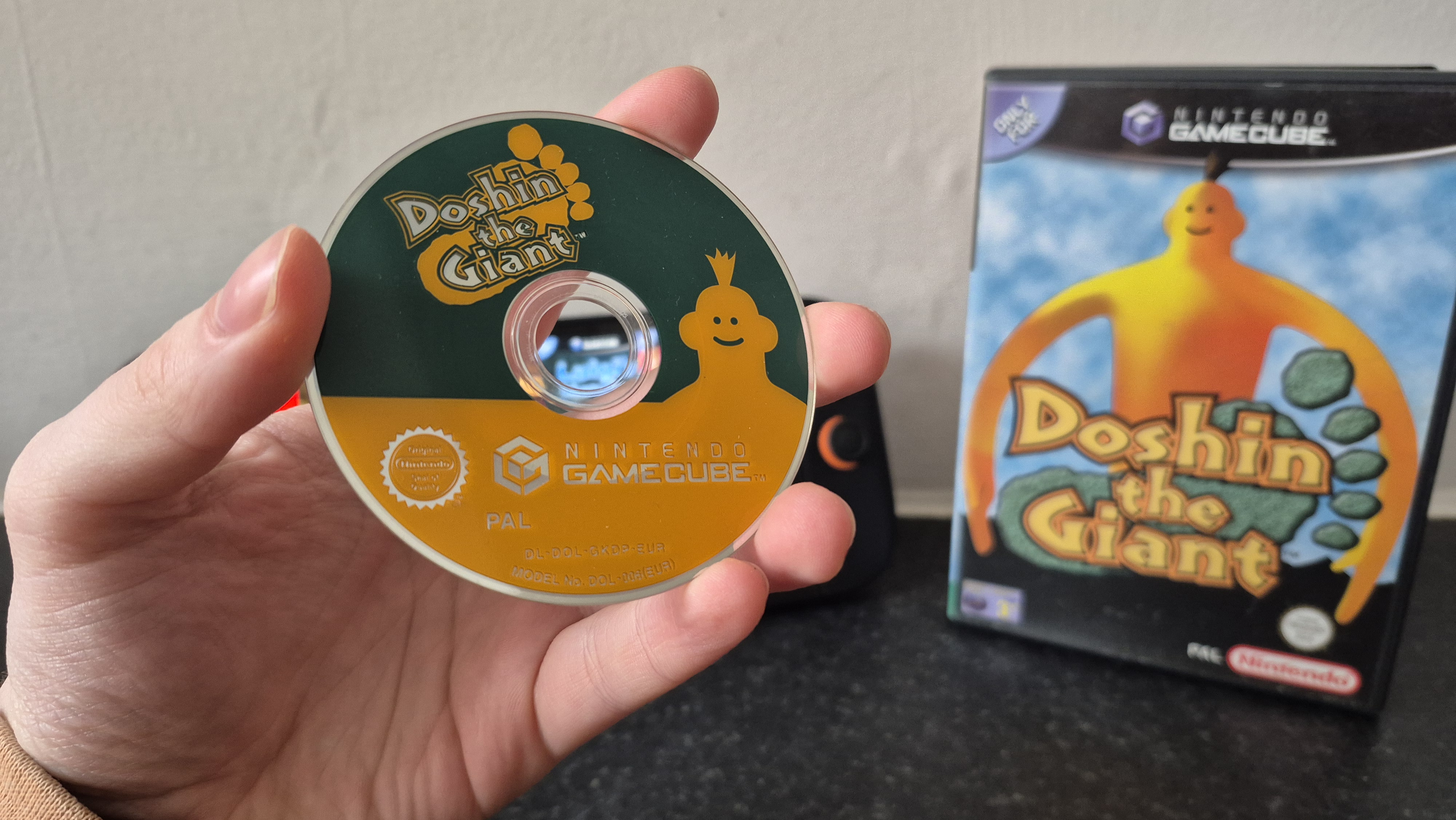 Man holding disc of Doshin the Giant with game case and Nintendo Switch 2 console in the background