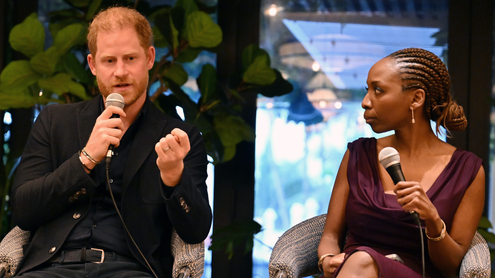 Prince Harry speaking into a mic sitting on stage next to Sophie Chandauka
