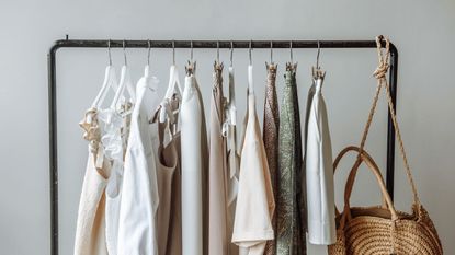 Some neutral colored clothing handing on a clothes rail in front of a plain white wall