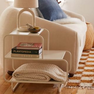Urban Outfitters side table with a shelf underneath with three stacked books, and a futher shelf under that with a folded knitted cream throw blanket
