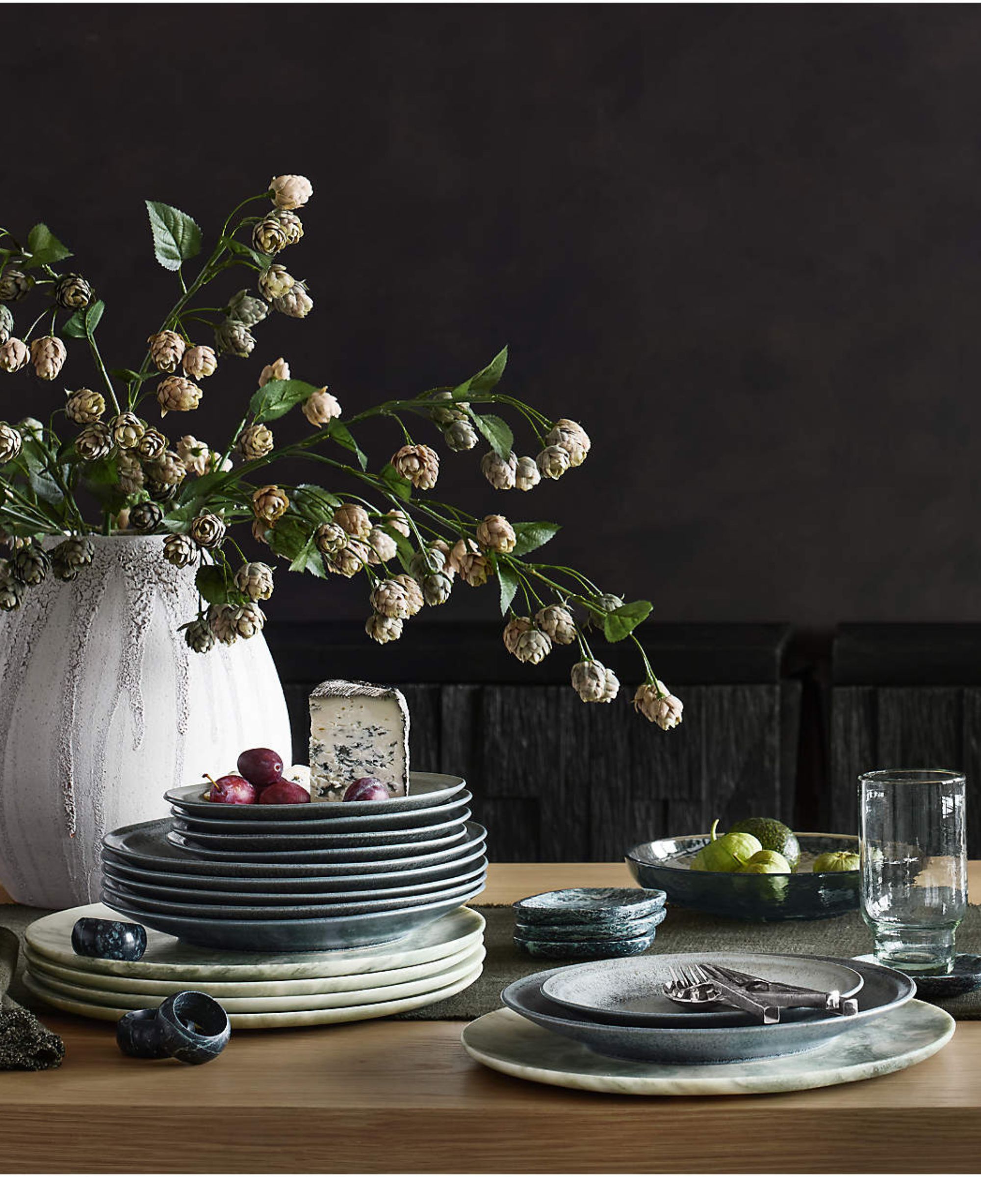 Oak table with cream and pale green stoneware plates, and a large white marble vase