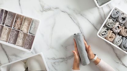 A woman folding clothes and underwear into drawer organizers on a marble worktop