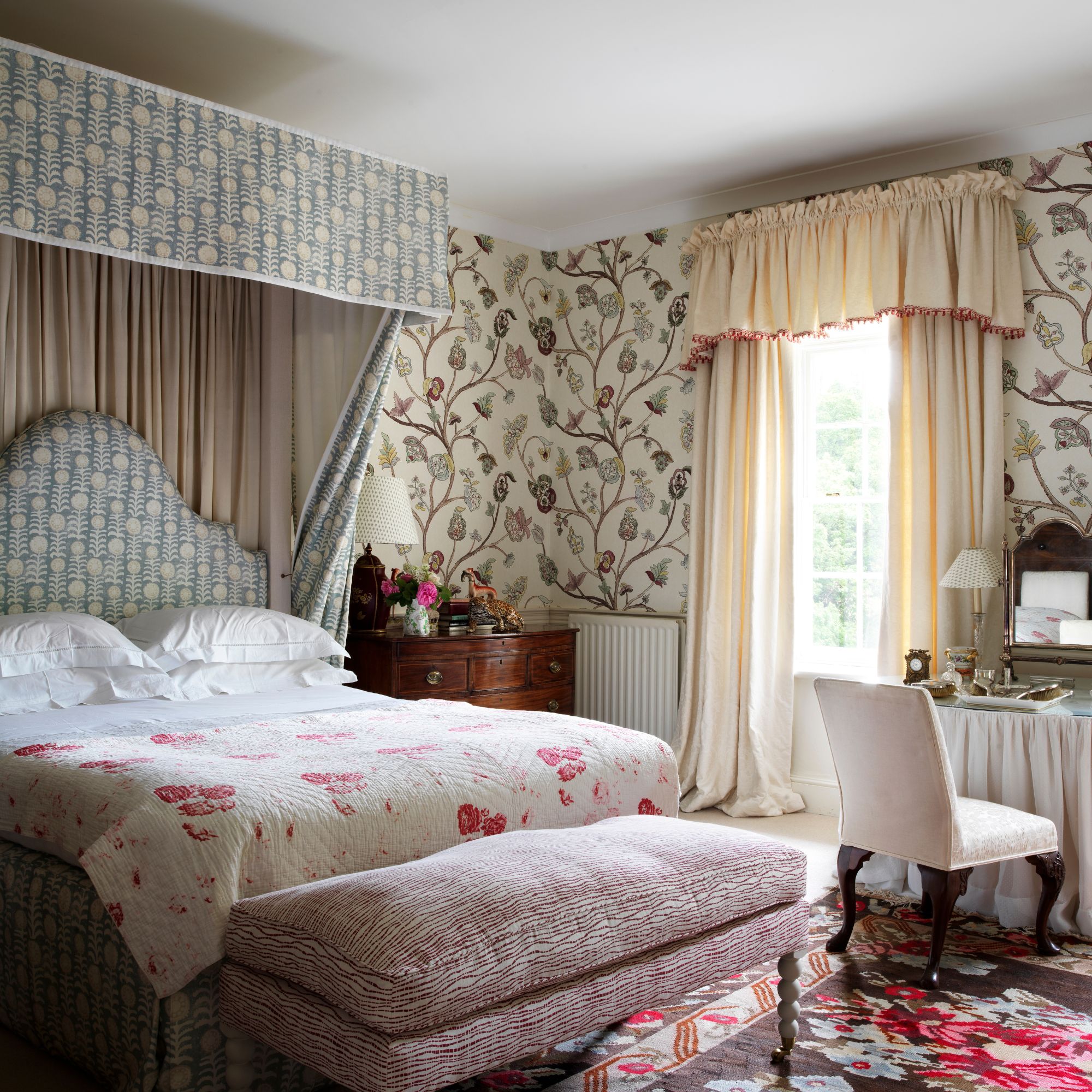 A floral, wallpapered French-style bedroom, filled with antique, patterned furniture.