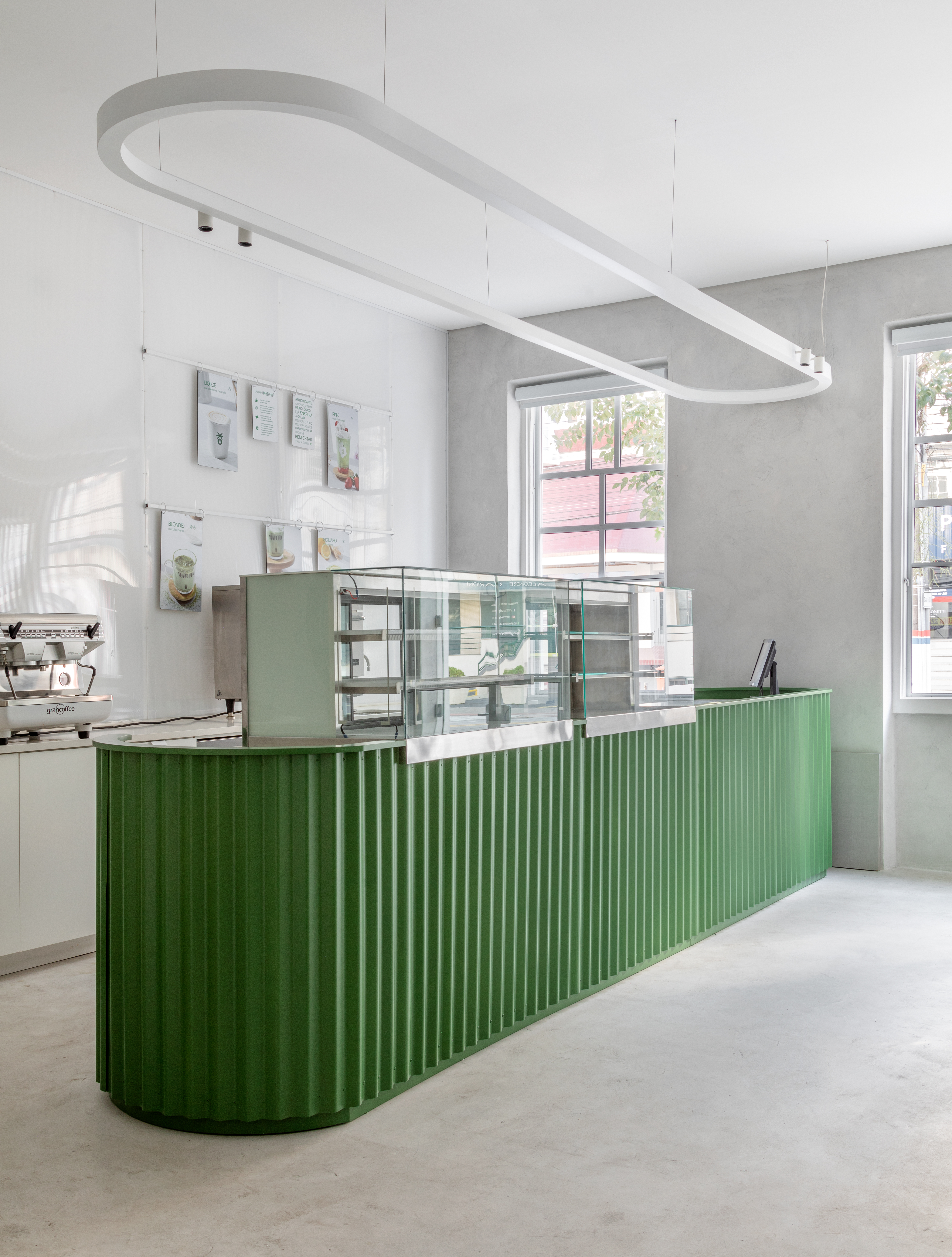 A white-washed, plastered matcha cafe with sculptural decor features monochromatic furnishings and an emerald green and chrome bar counter.