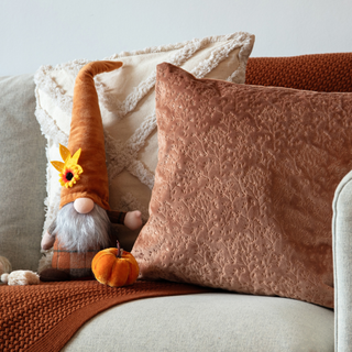 Autumnal gonk on sofa with red flowered cushion, cream sushion and orange throw