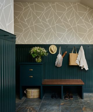 A mudroom with dark green paneling and geometric wallpaper