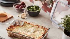 Vegetable lasagne in glass container next to bowls of herbs and spices