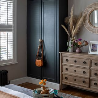 Bedroom with navy wardrobe and wooden chest of drawers, decorated with vases filled with flowers