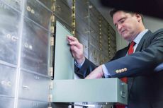 Mature man wearing a business suit opening a safety deposit box, looking inside.