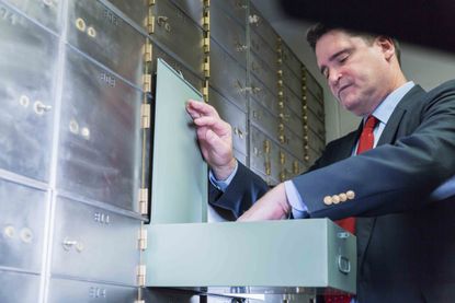 Mature man wearing a business suit opening a safety deposit box, looking inside.