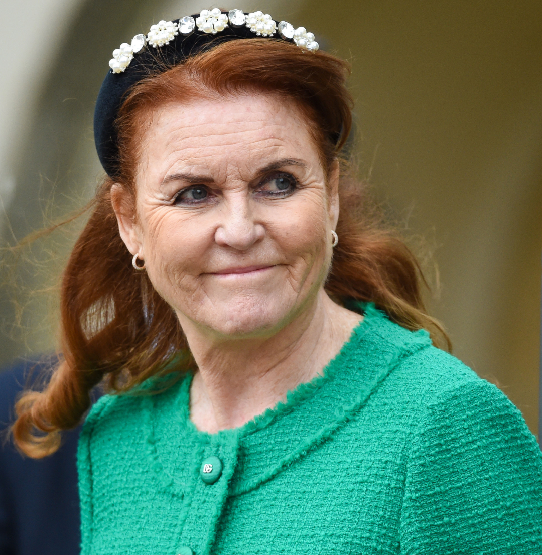 Sarah Ferguson wearing a green jacket and black headband looking to the side and smirking