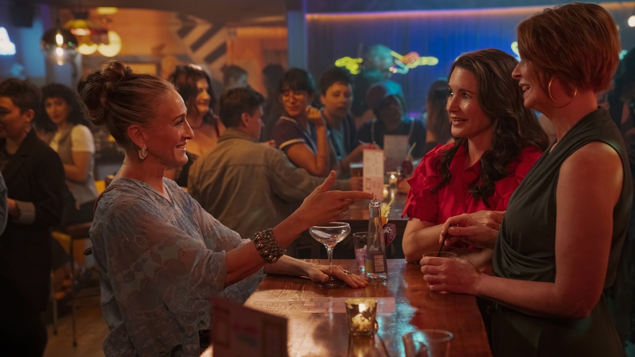 Carrie (Sarah Jessica Parker) knocking back cocktails in a warmly-lit bar with her Manhattan besties Charlotte (Kristin Parker) and Miranda (Cynthia Nixon) in And Just Like That Season 3