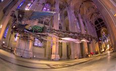 Ornate phoenix constructed from tools and debris from construction sites, hangs from the arched ceiling of a cathedral